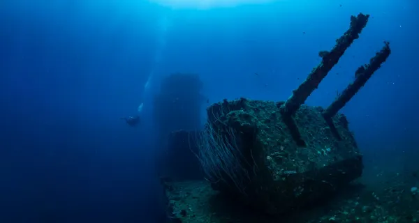 Scuba diver swimming near the gun turrets of a large World War II shipwreck lying deep underwater at Bikini Atoll, Marshall Islands.